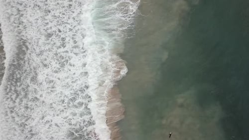 Stormy sea with waves breaking, white foam and beach sand dragged into the sea