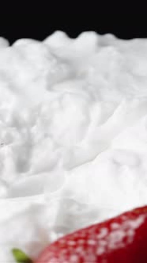 Vertical. A plate covered with a layer of whipped cream rotating, with strawberries falling