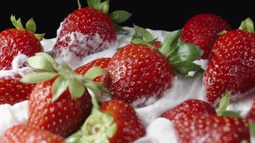A large plate with whipped cream and strawberries, slowly rotating. Dolly slider extreme close-up.