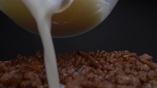 Moving close-up camera shot of woman pouring milk into cereals. Probe lens.