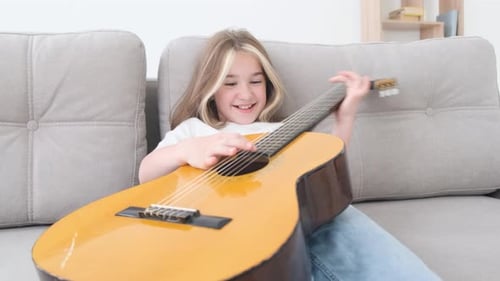 Young Girl Plays the Guitar on a Sofa