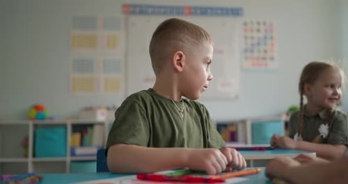 Young Children Sitting at Classroom Desks Talking and Learning Together During a Colorful School