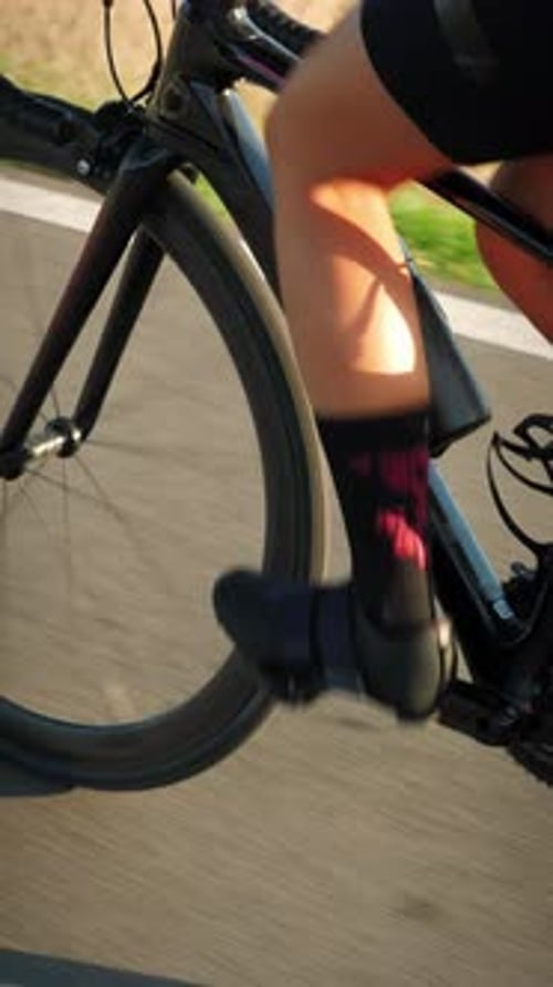 Nahaufnahme von Beinen in Fahrradschuhen beim Radfahren auf einer asphaltierten Straße. Vertikales Video