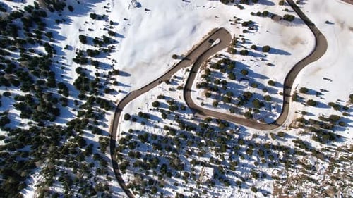 Captivating aerial view of a winding road cutting through a snowy forest, showcasing the intricate p