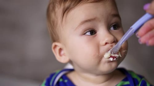 Sweet little kid nutrition. Mom gives a spoon with food to her child and cleans his mouth. Close up.