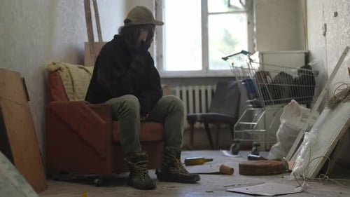 Homeless Poor Man Sitting in a Room of an Abandoned Building Filled with His Meager Belongings He