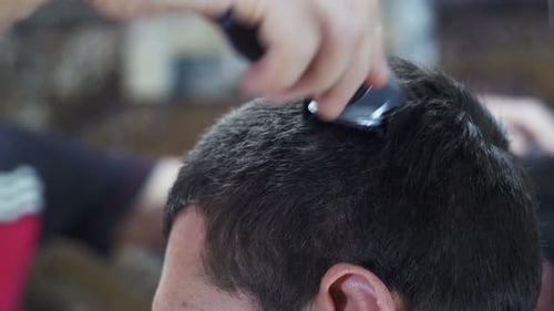 Peluquero corta el pelo de un joven con un cortaúñas en casa