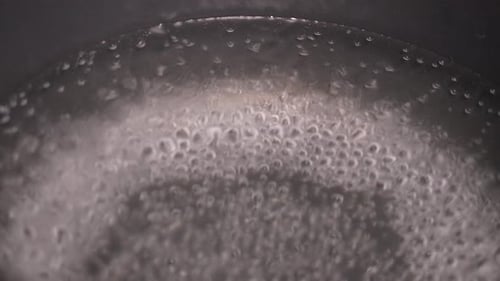 A pan of water is boiling and has a lot of bubbles. The bubbles are small and scattered throughout t