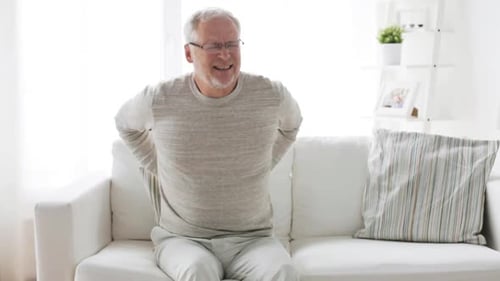 Senior man experiences back pain sitting on couch