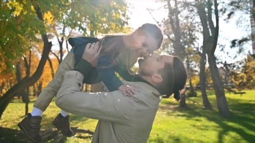 Happy family in an autumn park. Father lifted his daughter over his head and kissed her. Slow motion