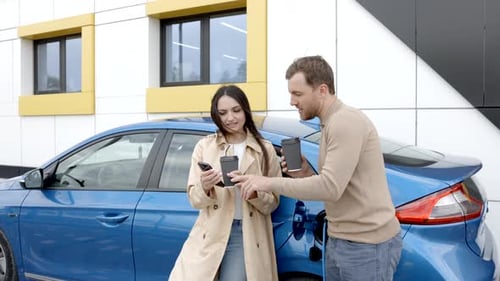 Young couple man and woman traveling by electric car having stop at charging station