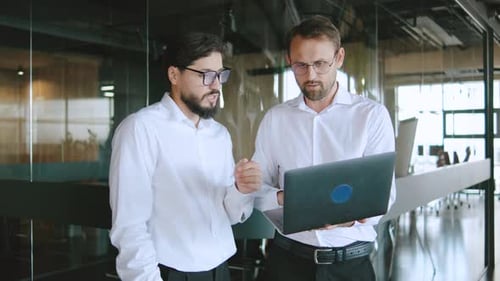 Two Men Discuss Work Tasks While Looking at a Laptop in a Modern Office During Daytime Meetings