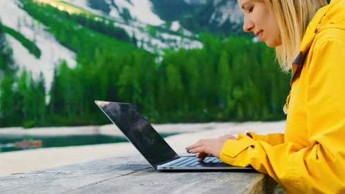 The Girl is Focused on Working at a Computer in Nature with a Beautiful View of the Mountains