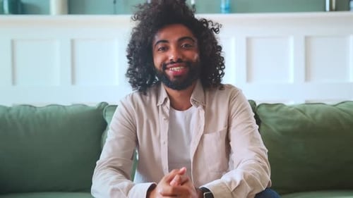 Young Happy Arabian Man Student with Curly Hair Smiling Sincerely Sits on Sofa