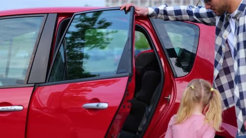 Young Father Opening the Car Door While Girl Sitting in the Car Seat in the Back Seat Family