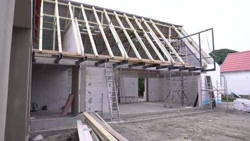 Estructura de la casa con vigas de techo expuestas, paredes de bloques de concreto y andamios en una construcción