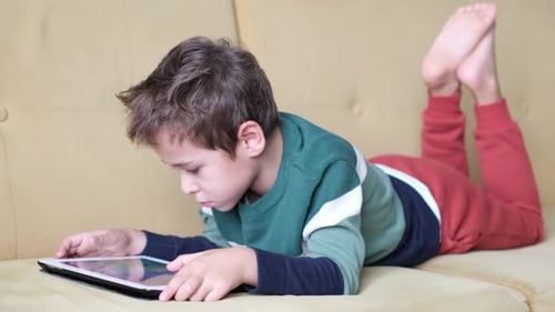 Child Plays on Tablet While Relaxing on Couch