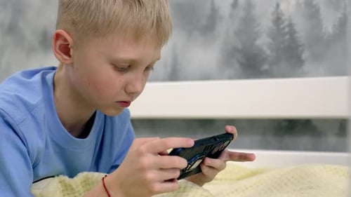 Boy Lying in Bed Playing Mobile Phone Game