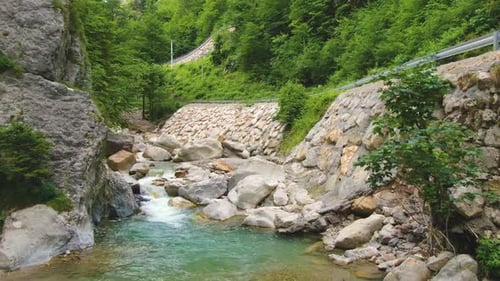 Shallow clear river with stones surrounded by rocks and greenery by the traffic road