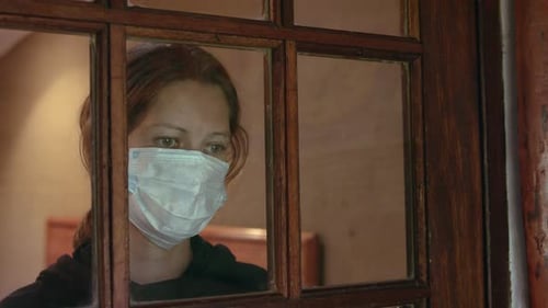 Woman Wearing Mask Behind Glass Window At Home