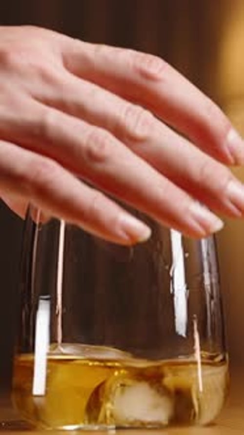 Pouring Glass of Golden Liquor Over Ice