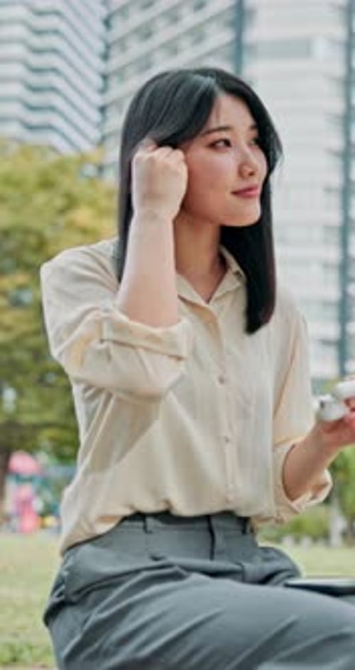 Business woman, earphones and music in park for break, streaming and relax with audio app