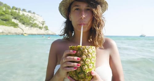 Beautiful young girl doing selfie at sea, drinking pineapple cocktail, in swimsuit in straw hat, b