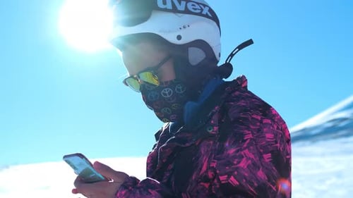 Skier Using Smartphone on Sunny Mountain Top