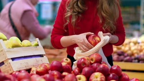 Mujer recogiendo manzanas en una bolsa reutilizable en una tienda. Temáticas del Día de la Tierra y la Ecología