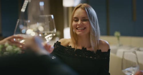 Close up of an elegantly dressed friends are clinking with wine glasses during a festive dinner at