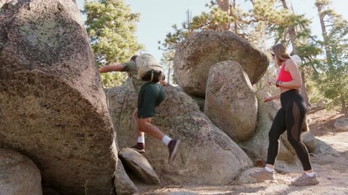 A Young Man with a Backpack And Young Woman Are Climbing Rocks In The Woods
