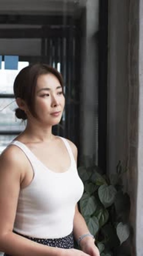 Vertical video: Standing confidently in modern office, businesswoman wearing white tank top and watc