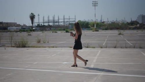 Young Girl Caucasian Woman in Short Black Dress Walking in Profile in Suburban Industrial Area Near