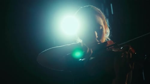 Woman Plays Violin on Stage in Dramatic Lighting