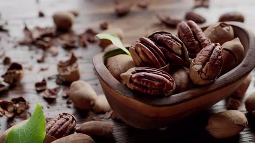 Pecans in a wooden bowl with pecan leaves and nut shells.
