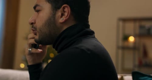 Thoughtful Young Adult Man Sitting Indoors at Christmas