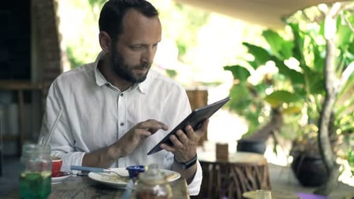 Young Man Browsing Internet on Tablet Computer Sitting in Cafe 30s