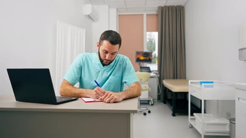 A doctor with a beard conducts an online consultation with a patient using laptop in his office