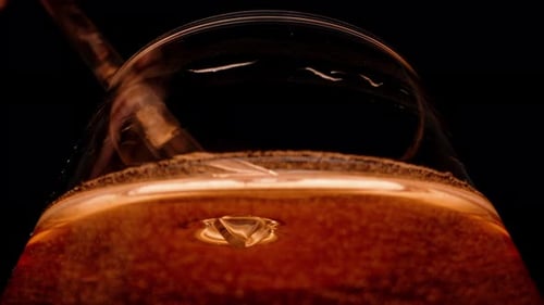 A transparent glass straw is submerged into a glass of red drink and sipped, slow-motion.