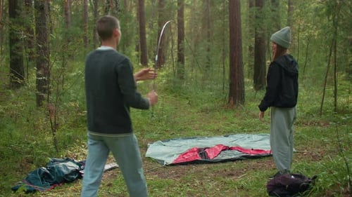Man Bending Tent Pole Toward Ground While Lady Observes During Camp Setup