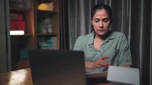 Woman Working on Laptop with Paper at Night