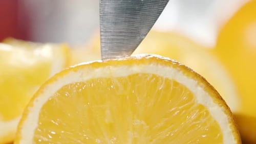 Closeup shot sharp knife slicing orange releasing Peel particles in the air, Slow motion