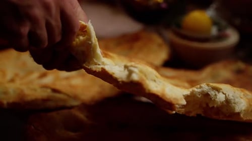 Gros plan d'un boulanger cassant un pain plat fraîchement cuit Le boulanger porte une chemise jaune et a