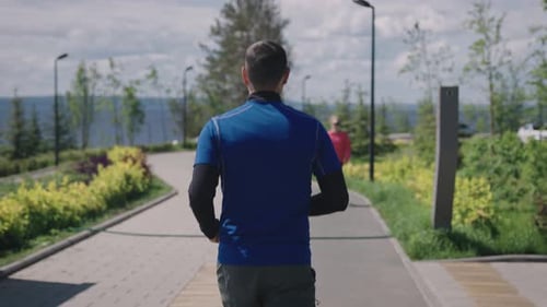 View From the Back A Man in Sportswear Runs Through a Landscaped City Park Public Urban Spaces for
