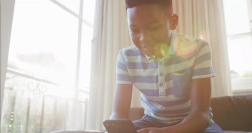 Boy Using Phone Sits in Brightly Lit Home