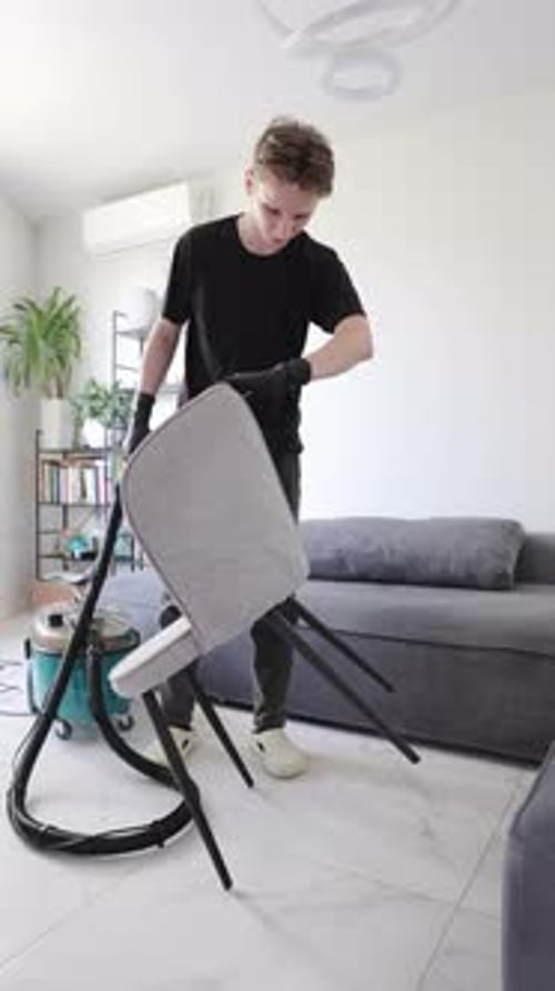 Young Man Cleaning Chair with Vacuum Indoors