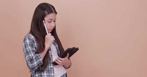 Schoolgirl using computer tablet to study and take notes. Isolated on brown background in studio.
