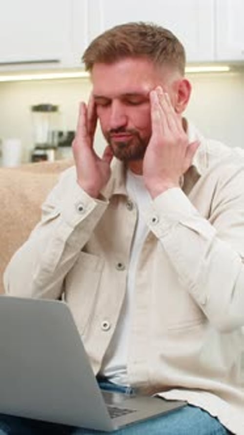 Man Massaging Temples While Working on Laptop at Home