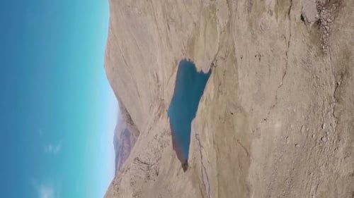 VERTICAL amazing view descending drone shot across grassland mountain range with lake at the bottom