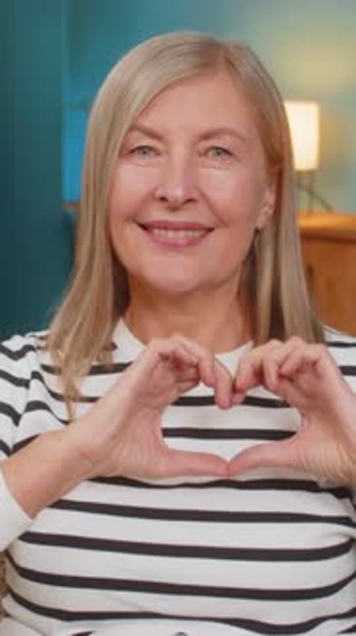 Smiling Woman Makes Heart Shape with Hands Indoors